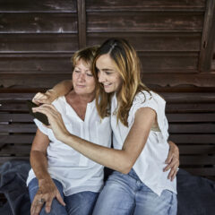 Mother and adult daughter on porch of a log cabin using smartphone