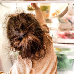 mixed-race toddler girl reaches for a healthy snack from refrigerator
