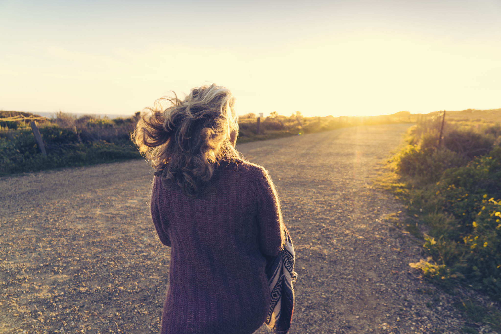 Rear view of woman walking on dirt road during sunset