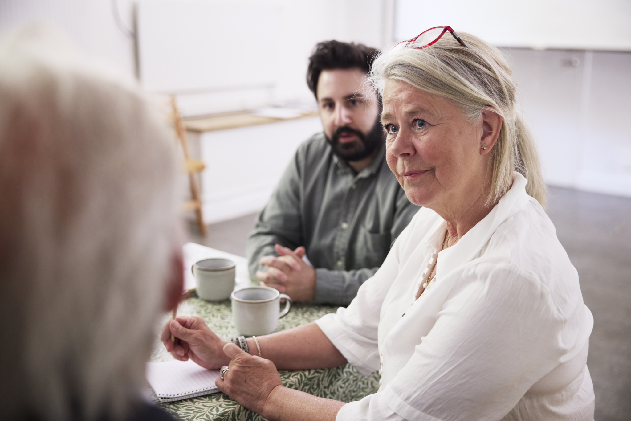 Smiling mature businesswoman with colleagues sitting at desk in office during meeting